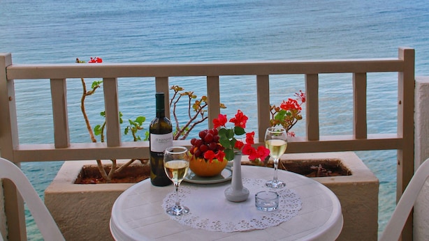 A table with a bottle of wine, a glass, and a bowl of grapes on a balcony overlooking the sea. - Maragakis Beach Hotel (Hersonissos)