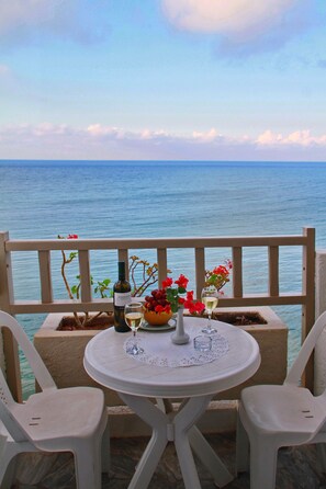 Una mesa con una botella de vino, una copa y un bol de uvas en un balcón con vistas al mar.