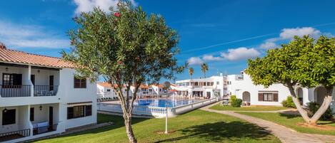 A courtyard with a swimming pool, white buildings with balconies, and a tree with pink flowers.