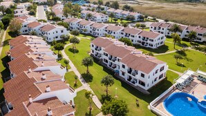A coastal resort with white buildings, red-tiled roofs, and a swimming pool. - Apartamentos Son Bou Gardens (Alayor)