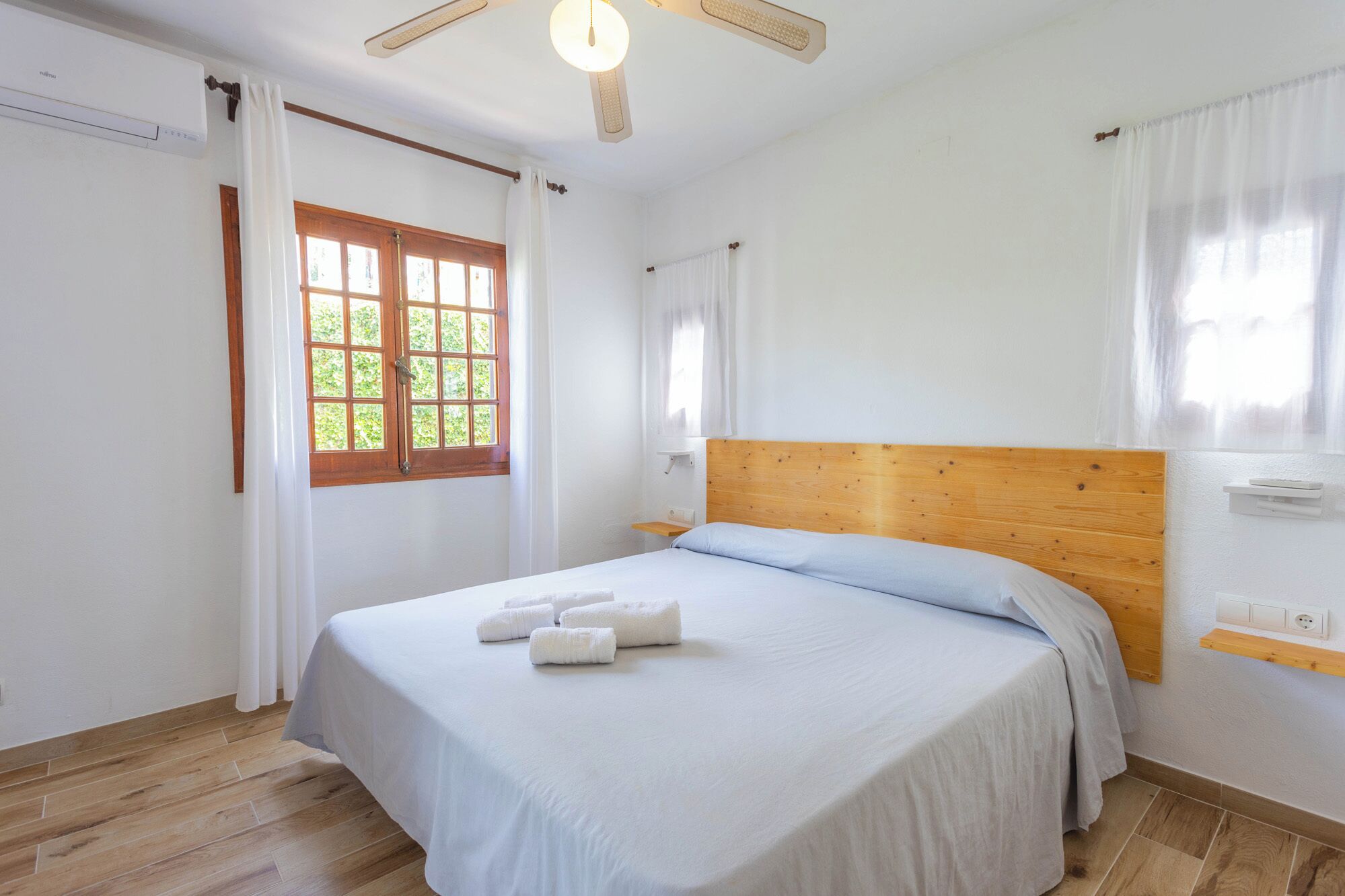 A bedroom with a wooden headboard, a bed with white bedding, and a window with wooden shutters.