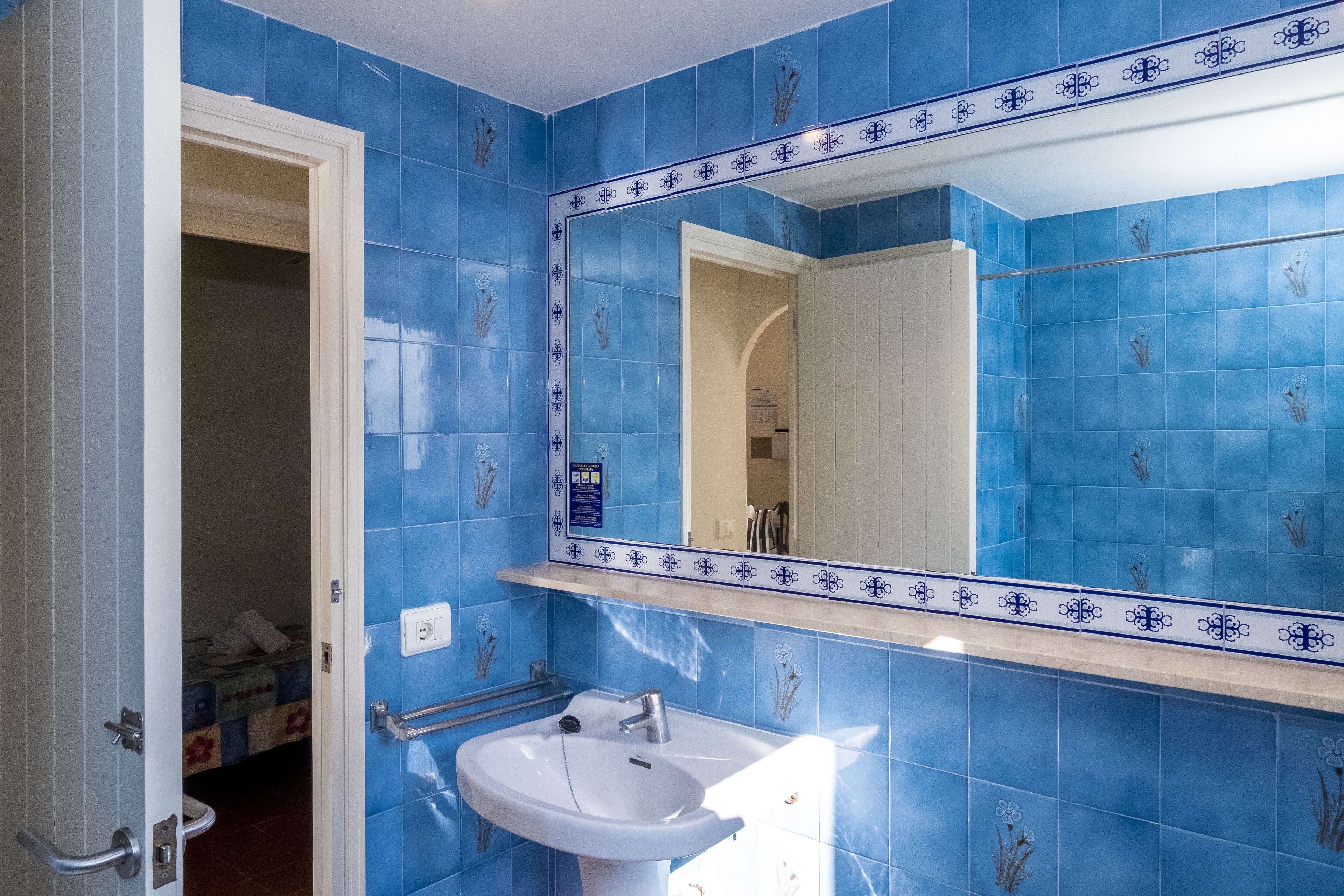 Un baño con azulejos azules, un lavabo blanco y un espejo con detalles decorativos.