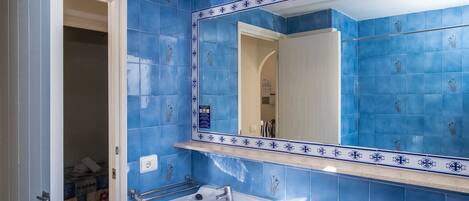 Un baño con azulejos azules, un lavabo blanco y un espejo con detalles decorativos.