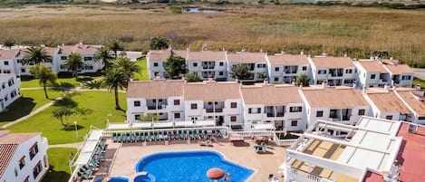 A hotel with multiple white buildings, a swimming pool, and a view of the ocean.
