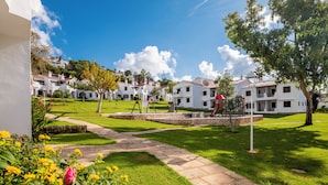 A courtyard with white buildings, a stone pathway, and a small fountain. - Apartamentos Son Bou Gardens (Alayor)