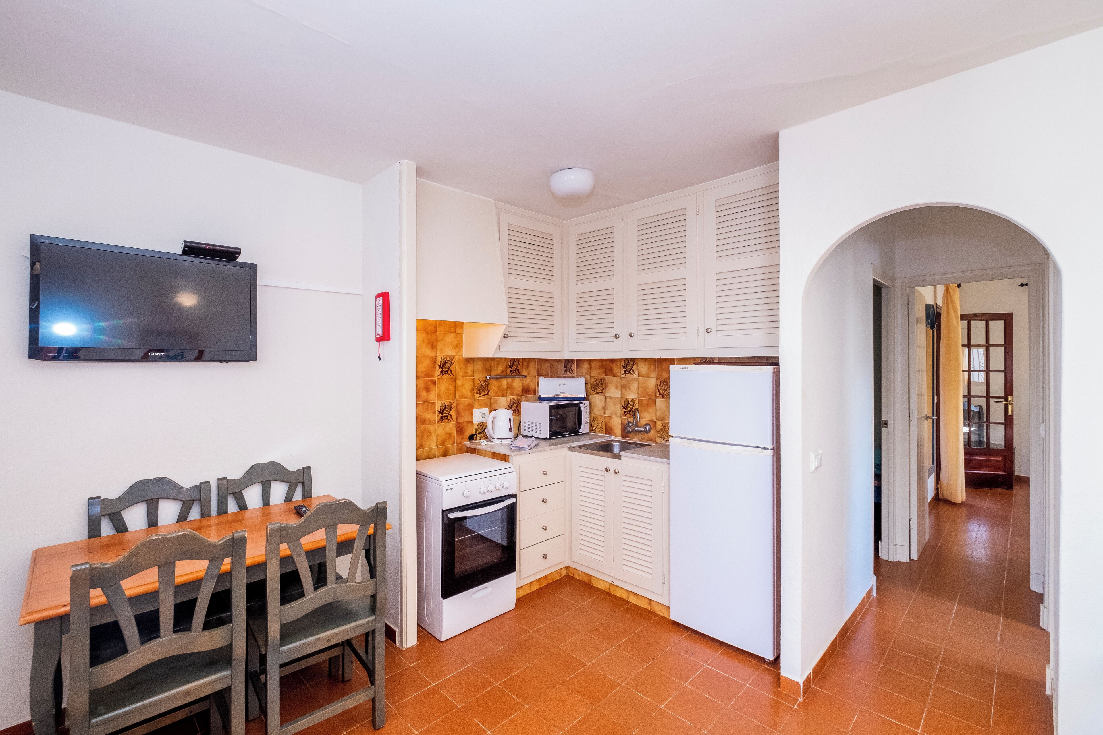 A compact kitchen with a dining table and chairs, a microwave, oven, and a refrigerator.