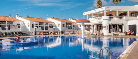 A swimming pool with a tiled deck, lounge chairs, and a building with a balcony.