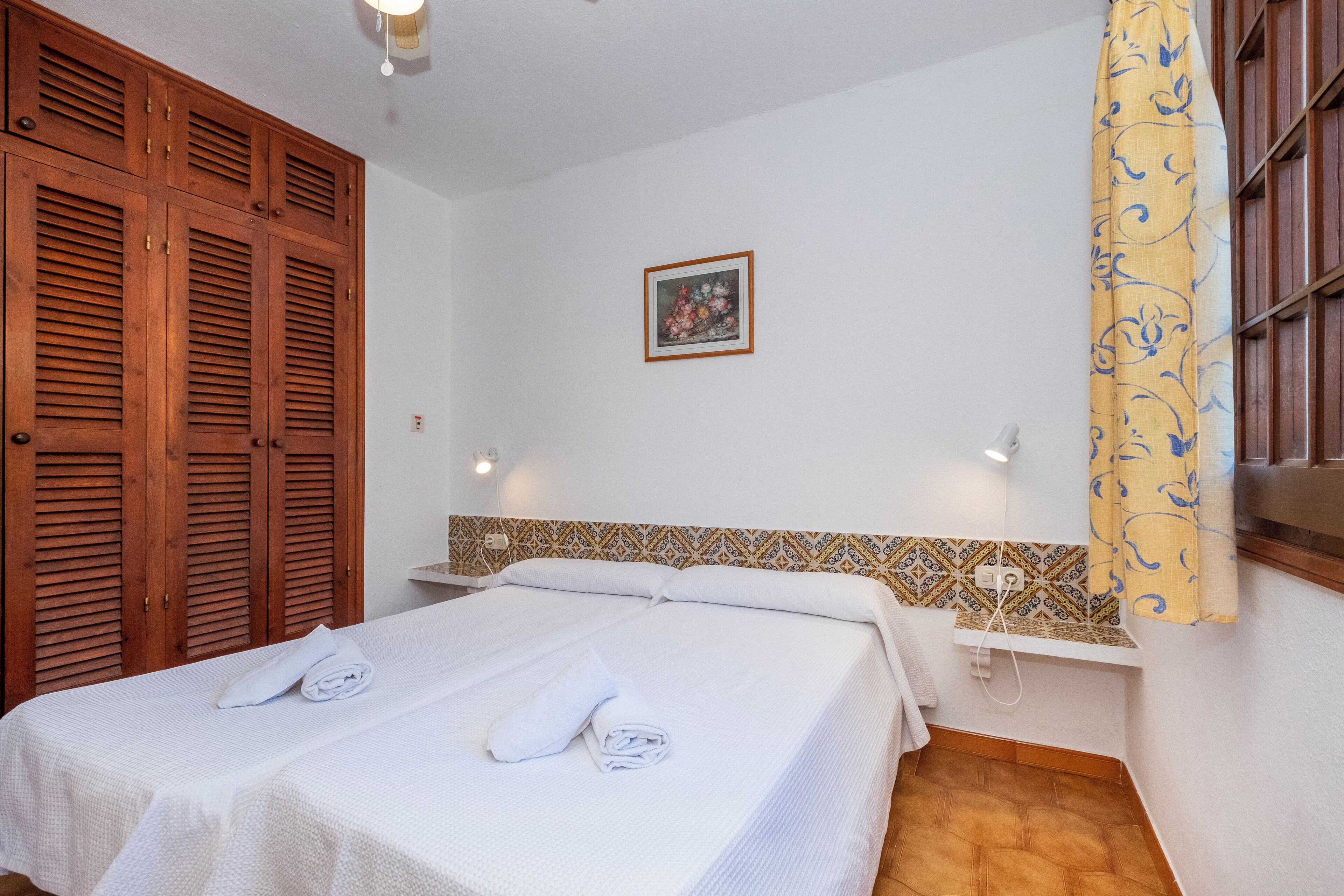 A hotel room with a bed, a wardrobe, a wall-mounted shelf, and a patterned tile backsplash.
