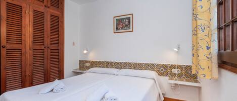 A hotel room with a bed, a wardrobe, a wall-mounted shelf, and a patterned tile backsplash.