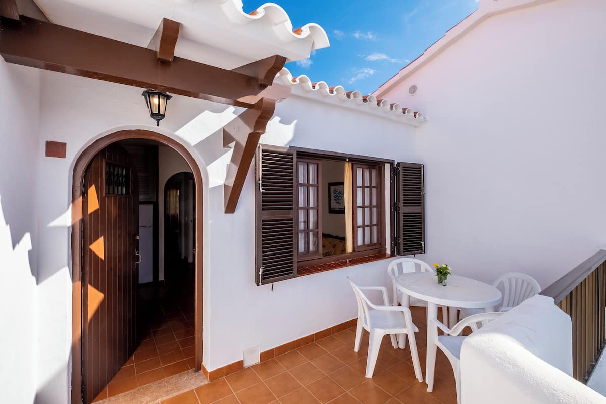 A white building with a covered patio area, a small table with chairs, and a door leading to an interior space.