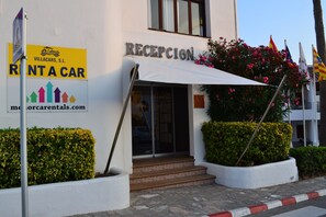 Un bâtiment comprenant un espace d’accueil, une enseigne indiquant « Location de voitures » et une adresse de site web.