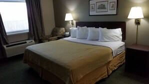 A hotel room with a large bed, two bedside lamps, a chair, a phone, and a window with curtains.