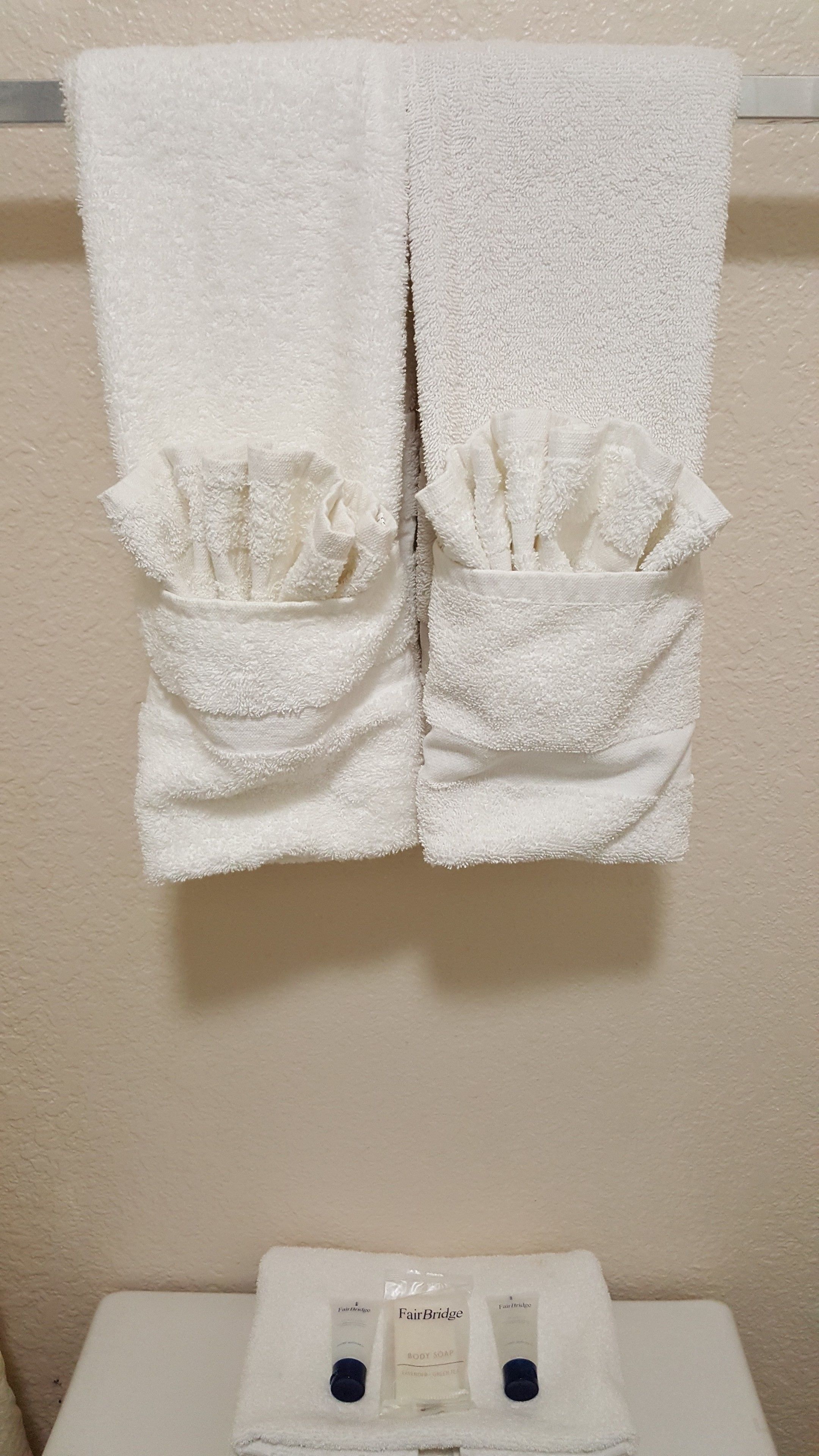 A bathroom with two white towels hanging on a towel rack, a white sink, and two bottles of FairBridge body soap.