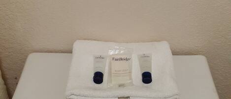 A bathroom with two white towels hanging on a towel rack, a white sink, and two bottles of FairBridge body soap.