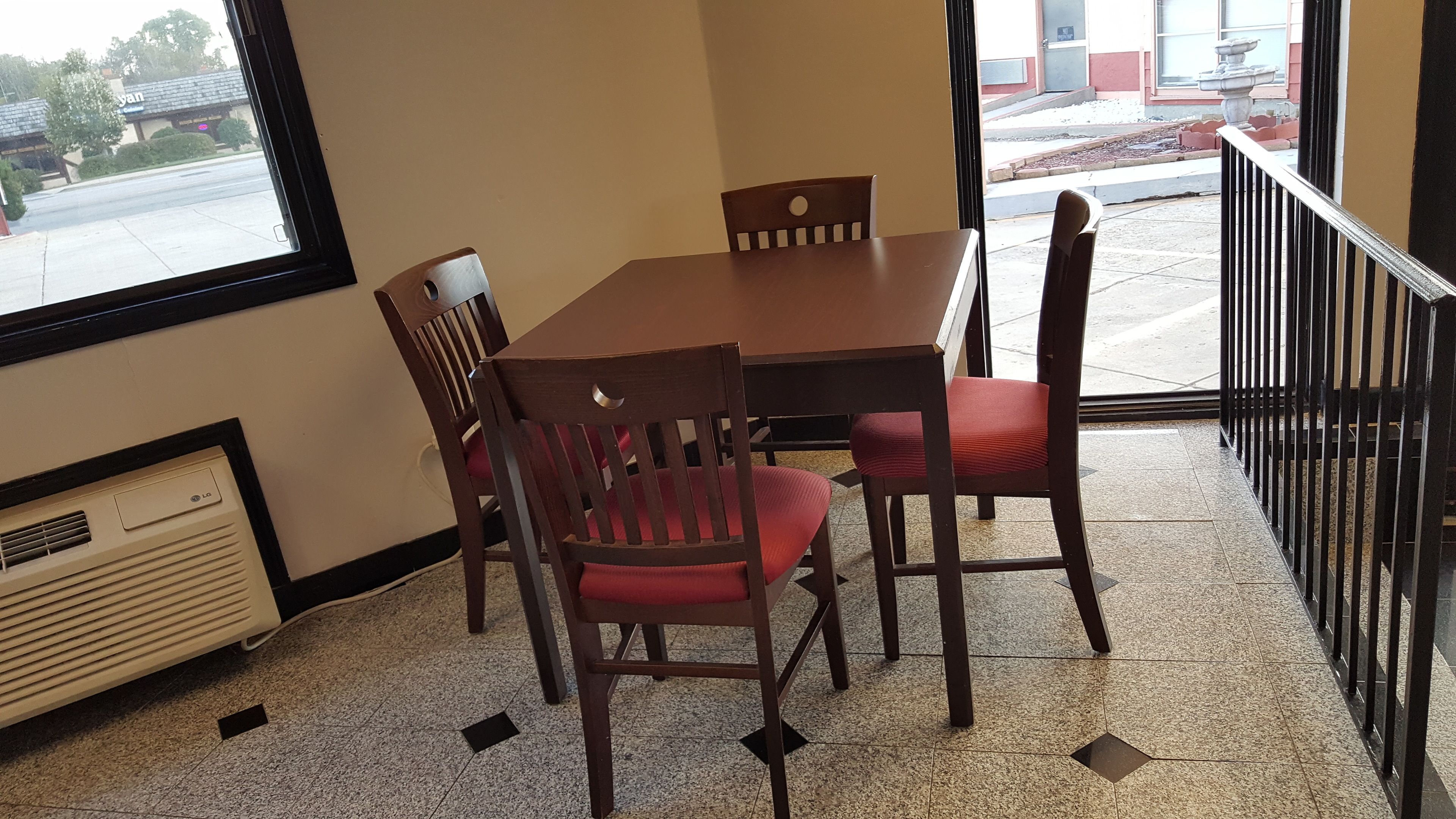 A dining area with a table and four chairs, a window with a view of the street, and a radiator on the floor.