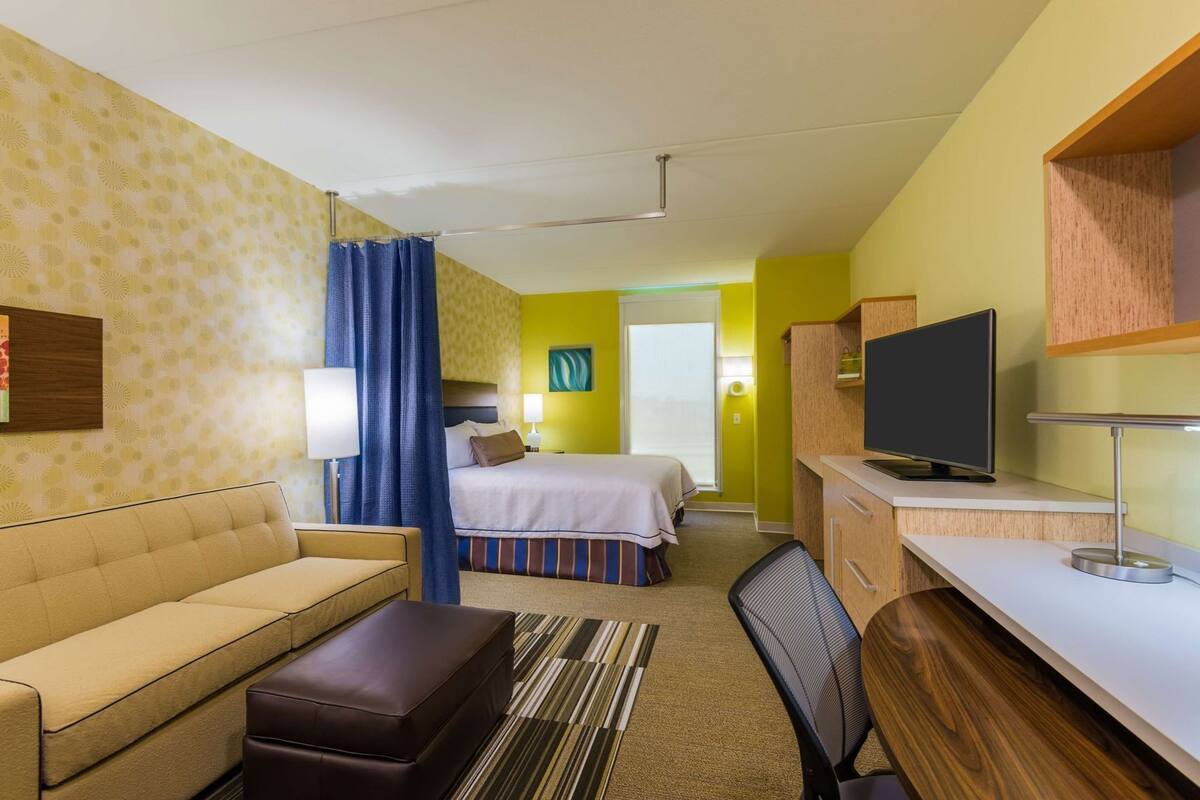 Ett hotellrum med en säng, en soffa, ett skrivbord, en tv och ett badrum som syns genom en öppen dörr.