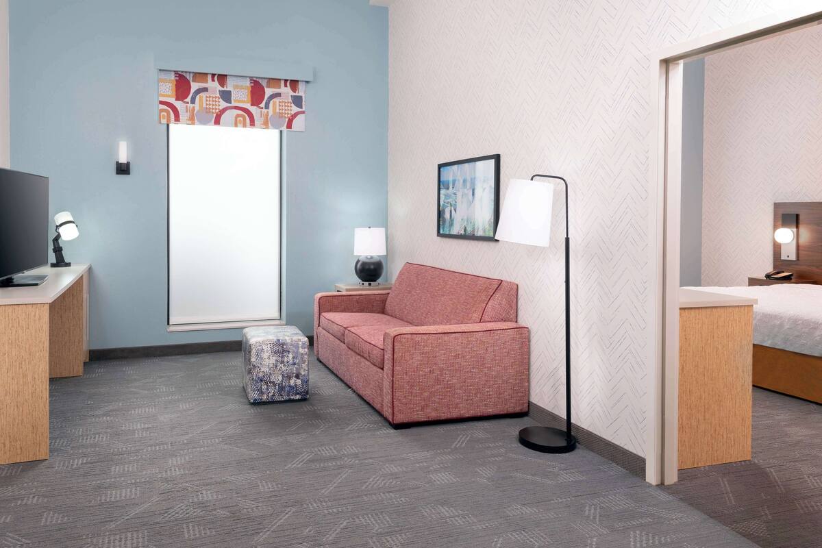 Ett hotellrum med en soffa, ett litet bord med en lampa, en tv och en säng.