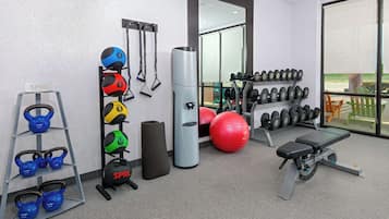 A gym with kettlebells, medicine balls, dumbbells, a bench, and a large mirror.
