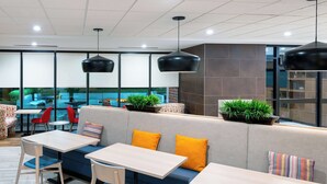 A modern indoor seating area with tables and chairs, a sofa with cushions, and hanging pendant lights.