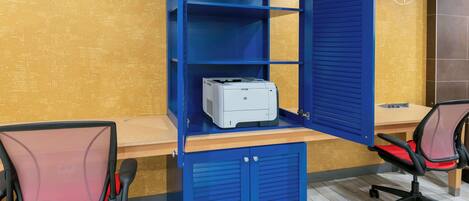 A blue office desk with a printer, two mesh chairs, and a wooden desk.