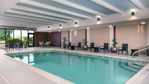 An indoor swimming pool with tiled flooring, seating areas, and potted plants.