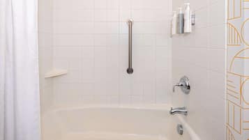 A bathroom with a bathtub, a handrail, and toiletries on the wall.