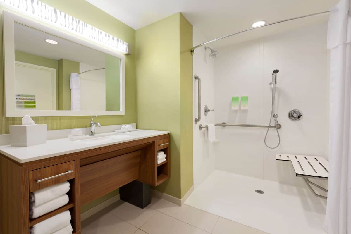 A modern bathroom with a wooden vanity, a large mirror, a shower with a glass door, and a white sink.