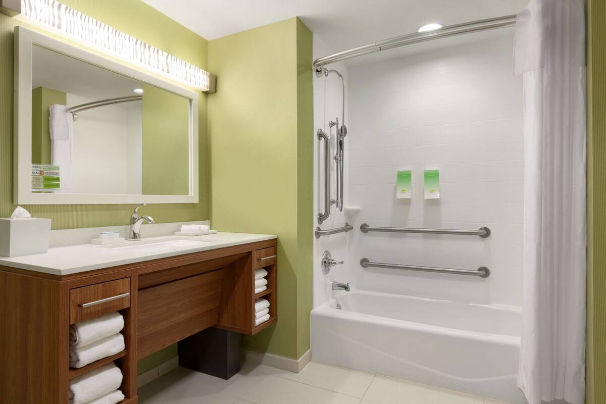 A bathroom with a wooden vanity, a large mirror, a bathtub with grab bars, and a shower area.