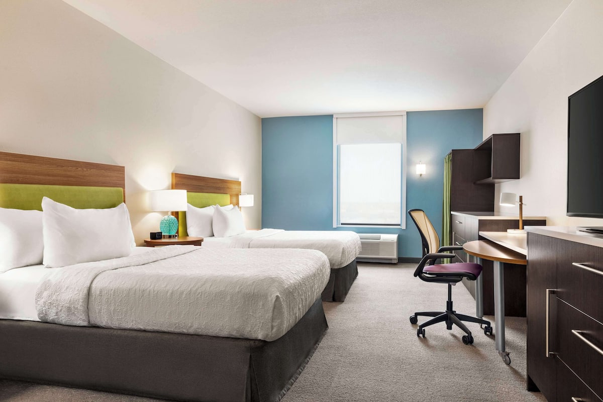 A hotel room with two beds, a desk, a chair, and a TV.