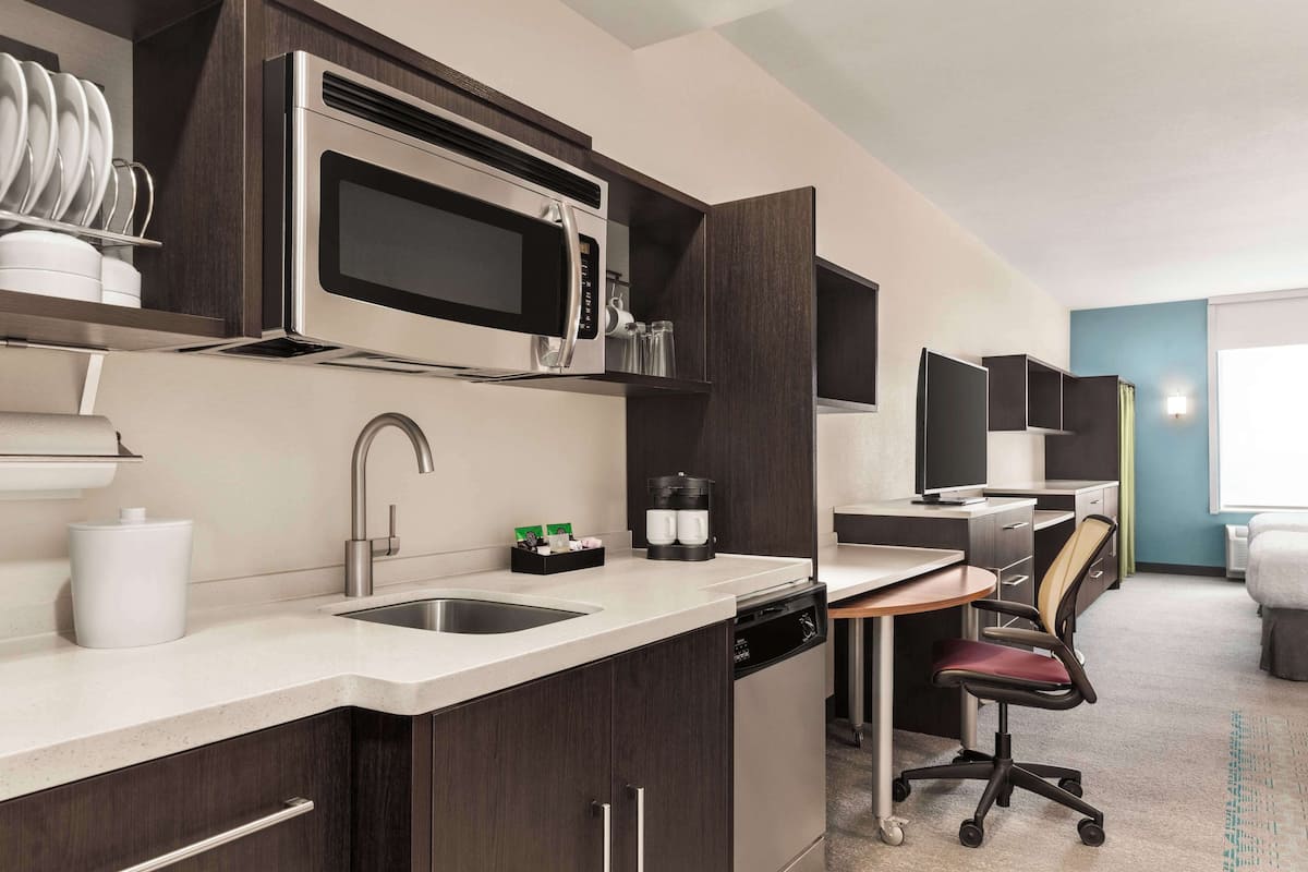 A modern kitchen with a built-in microwave, sink, and dishwasher. There is a small dining area with a chair and a table.