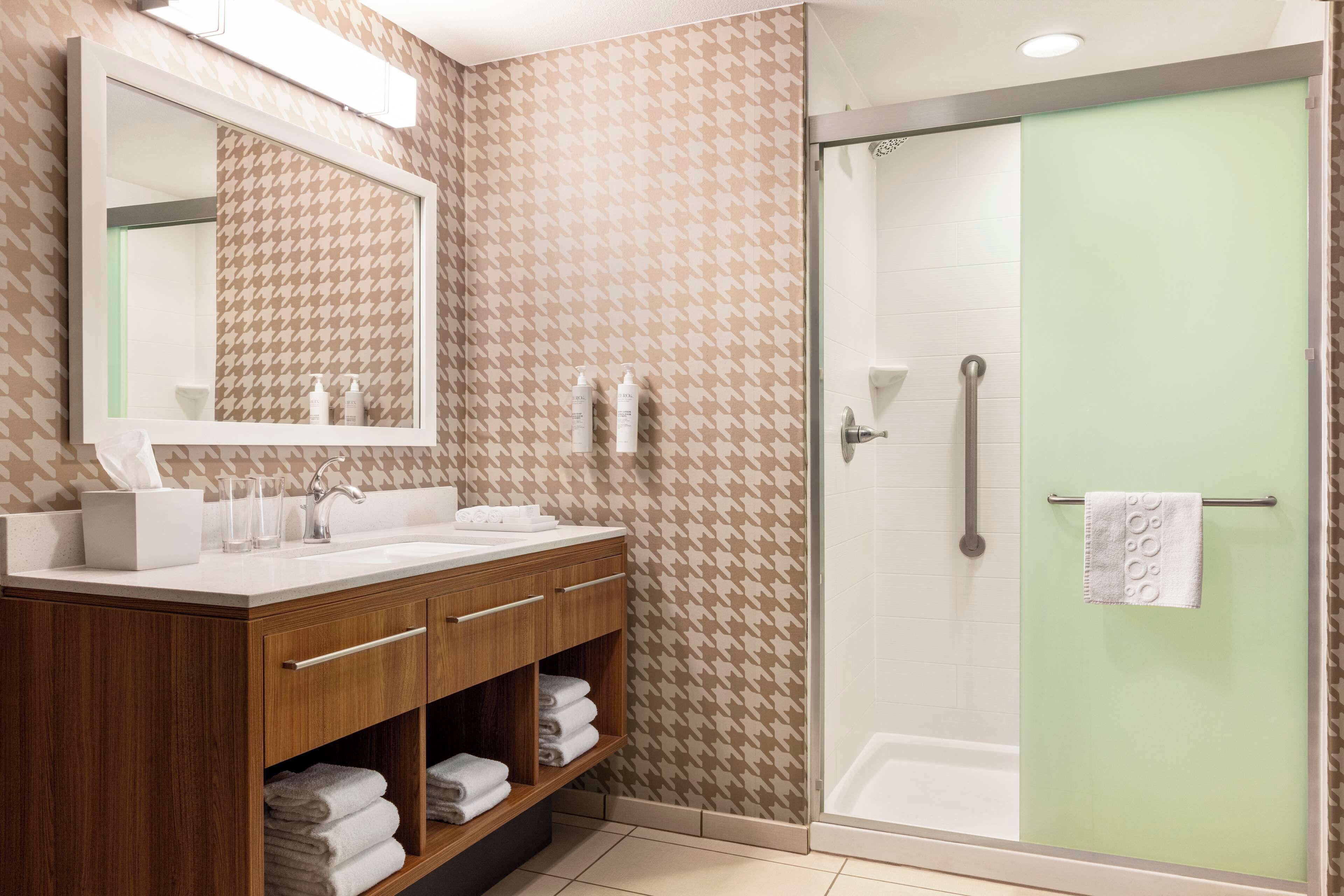A bathroom with a wooden vanity, a large mirror, and a glass-enclosed shower.