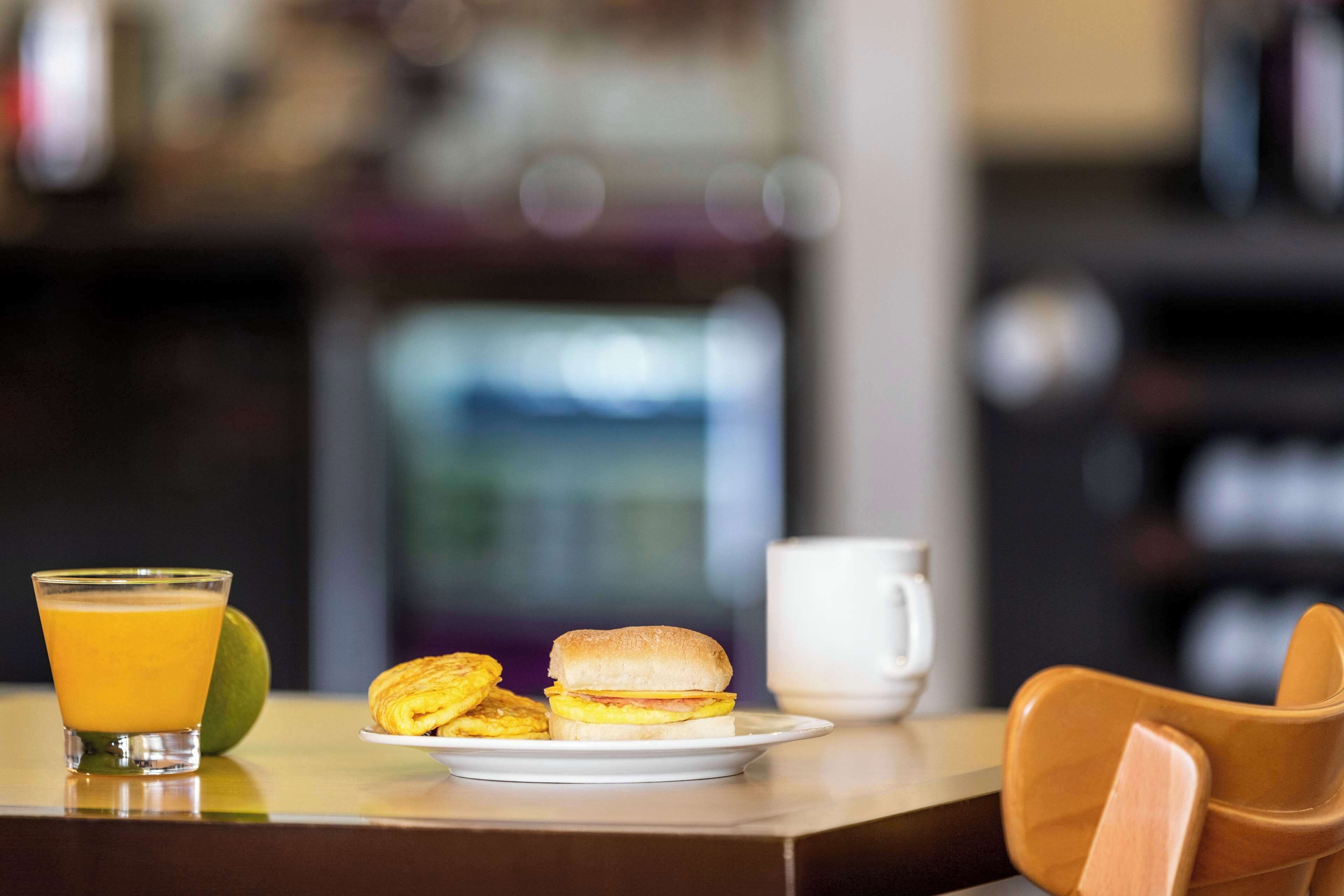 A breakfast setting with a glass of orange juice, a plate with a sandwich and pastries, and a white mug on a table.