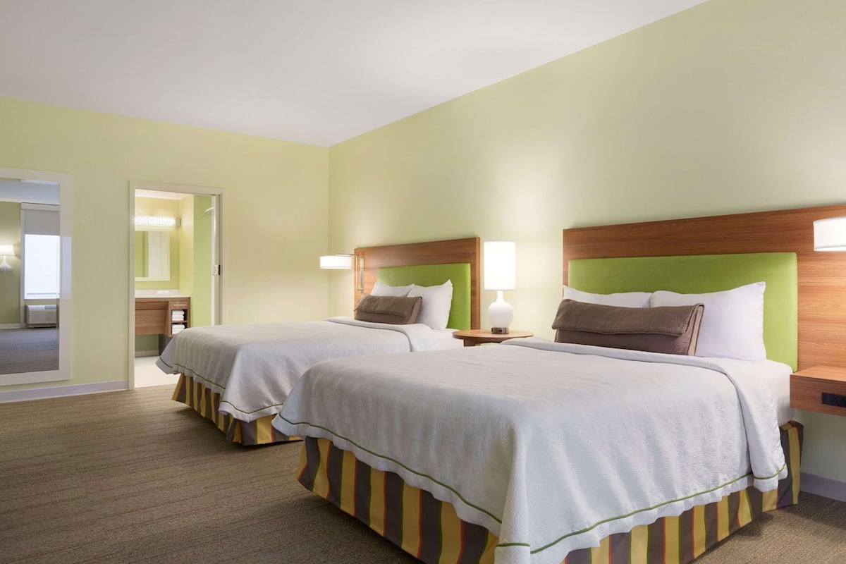 A hotel room with two beds, a bathroom, and a view of the outside.
