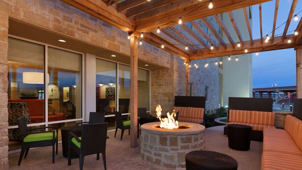 An outdoor patio with stone walls, a fire pit, wicker furniture, and string lights. - Home2 Suites by Hilton Lubbock (Lubbock)