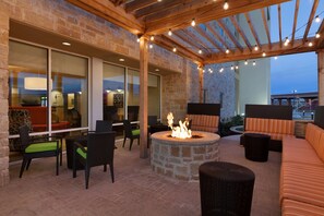 An outdoor patio with stone walls, a fire pit, wicker furniture, and string lights. - Home2 Suites by Hilton Lubbock (Lubbock)