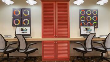 Un espacio de trabajo con dos escritorios, cada uno con una computadora y una silla. Hay dos armarios rojos y una pared decorada con obras de arte circulares.