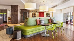 A modern lounge area with a green sofa, a small table, and green chairs. There are vending machines and a red door in the background. - Home2 Suites by Hilton Lubbock (Lubbock)