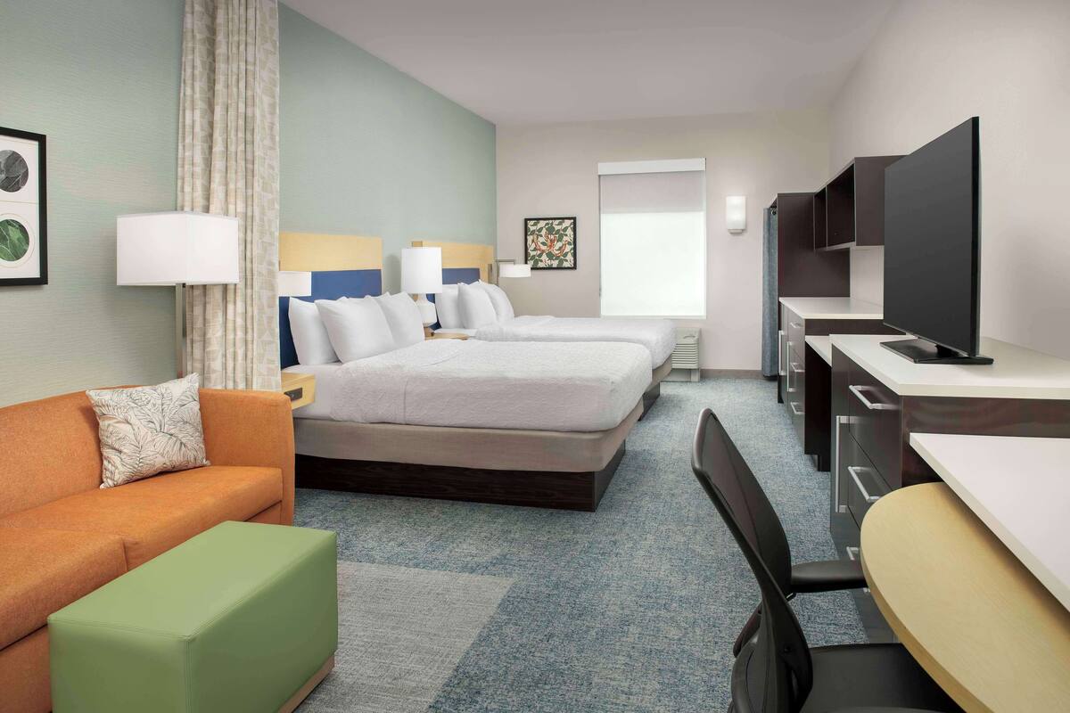 A hotel room with two beds, a sofa, a desk, a television, and a window with a view.