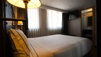 Een hotelkamer met een groot bed, een bedlampje, een aan de muur bevestigde televisie en een raam met gordijnen.