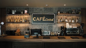 Un café con un cartel que dice "CAFÉ Central" sobre un mostrador con una máquina de café, un microondas y varias botellas.