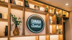 Una estantería de madera con un letrero de neón que dice "Canada Central" y varios libros y objetos decorativos.