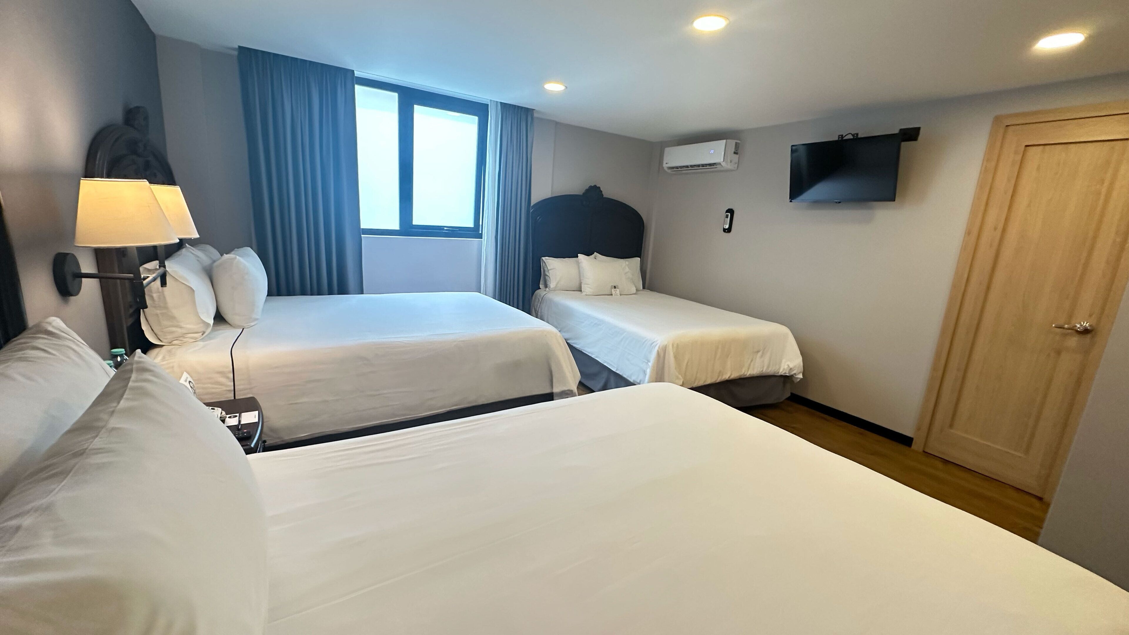 A hotel room with two beds, a flat-screen TV, an air conditioning unit, and a wooden door.