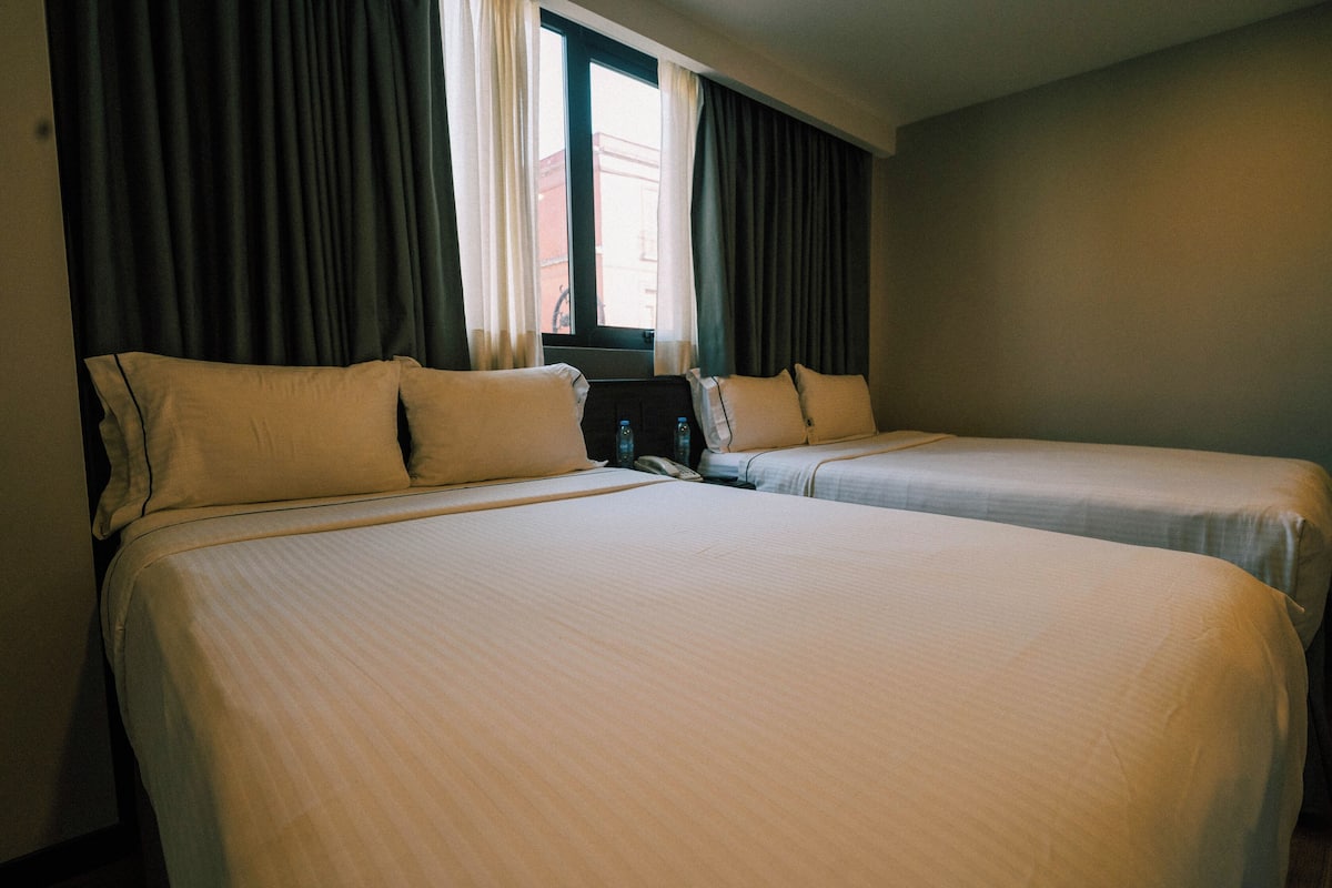 A hotel room with two single beds, a window with curtains, and a telephone on the nightstand.