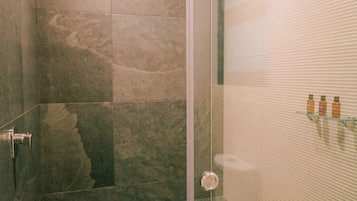 Un área de ducha con paredes de vidrio, suelo de baldosas y puerta de cristal.