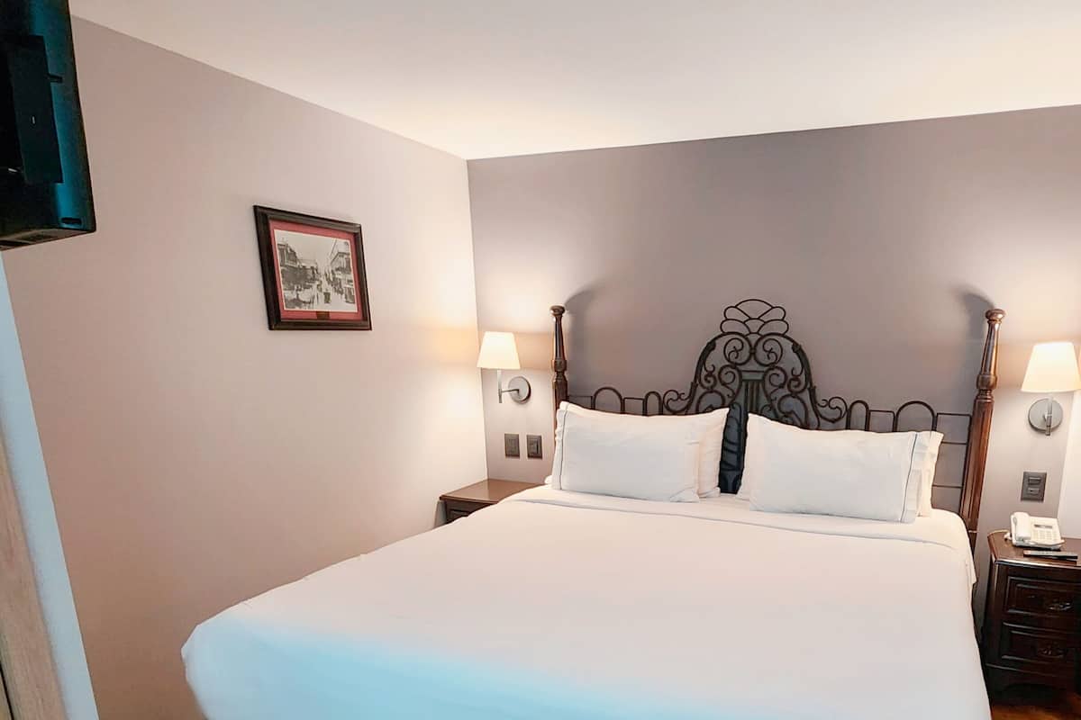 A neatly made bed with a white and blue bedspread, two bedside tables with lamps, a framed picture on the wall, and a wooden floor.