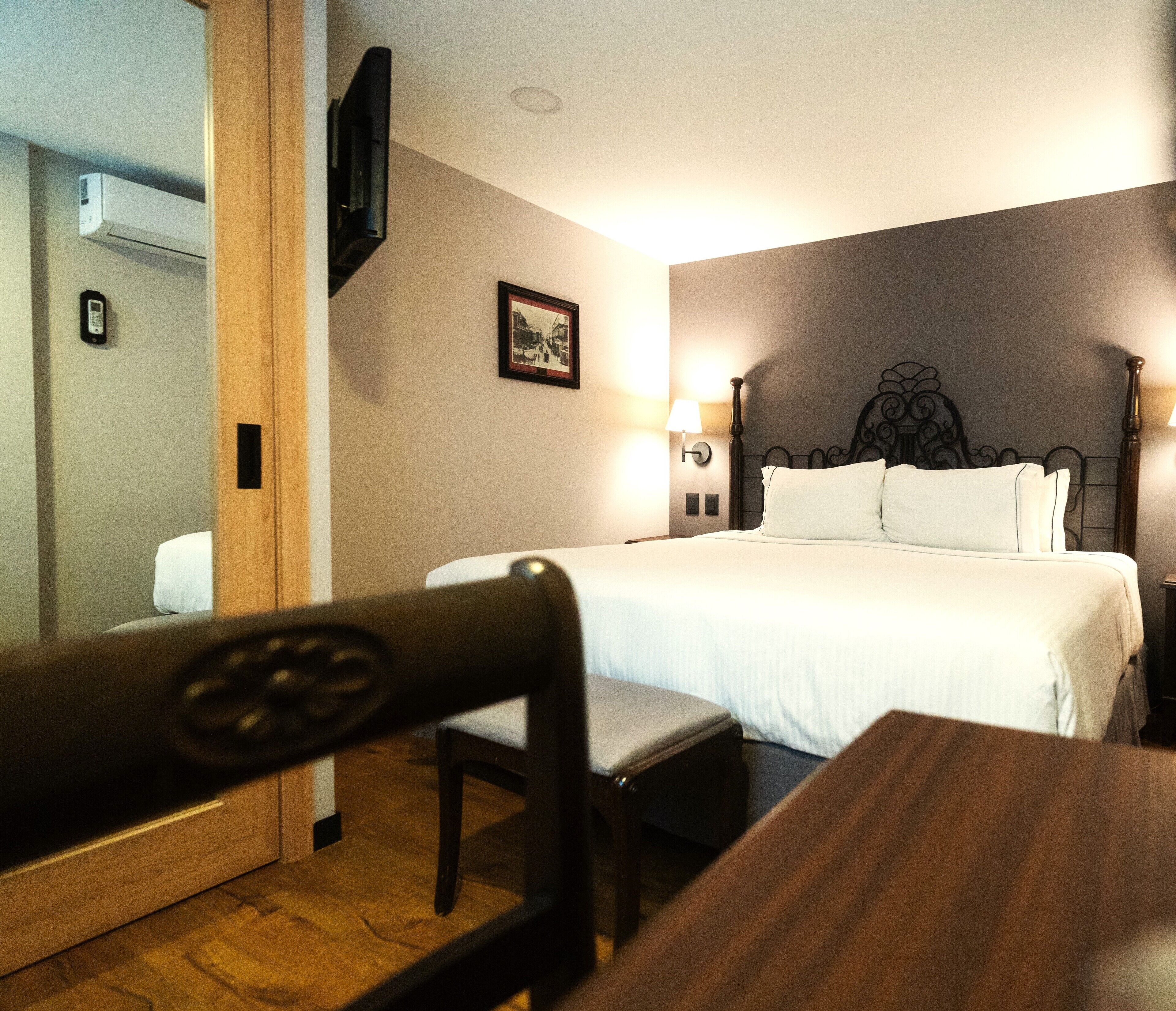Una habitación de hotel con cama, lámparas de noche, un cuadro en la pared y una silla de madera.