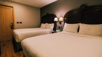 A hotel room with two beds, a wooden door, a nightstand with a lamp, and a wall-mounted phone.