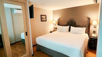 Quarto de hotel com uma cama grande, soalho de madeira, uma porta e um espelho.