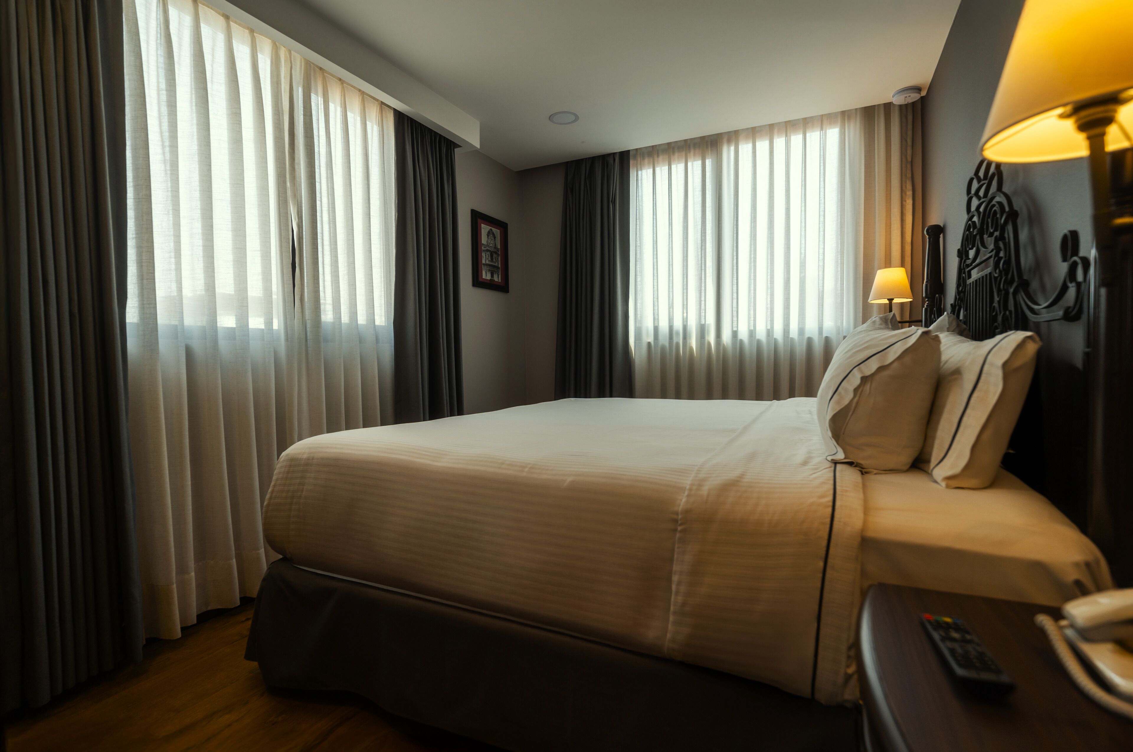 Una habitación de hotel con una cama grande, una mesita de noche con lámpara y cortinas en las ventanas.