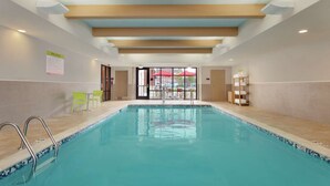 An indoor swimming pool with clear blue water, surrounded by beige tiles and a tiled border. There are metal pool ladders on the left side.